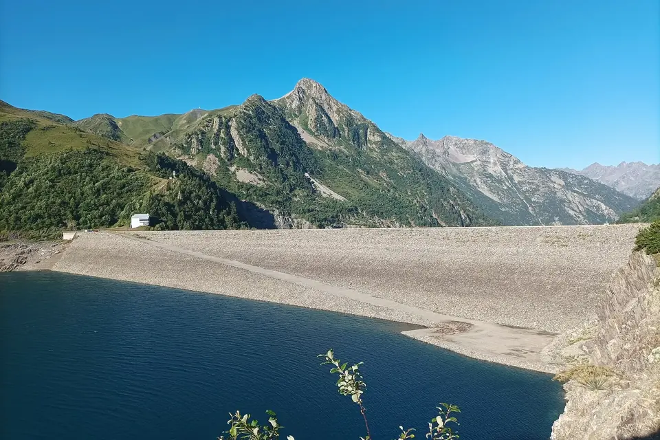 Le lac de retenue de Grand'Maison au pied de sommets alpins, avec le barrage en remblai à droite