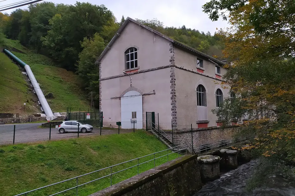 Bâtiment d'une petite centrale hydroélectrique au pied d'une conduite forcée qui descend la pente boisée