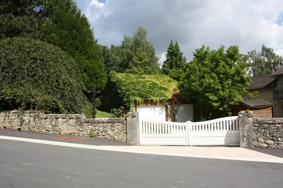 Maisons individuelles derrière des haies et un portail blanc dans une rue de village