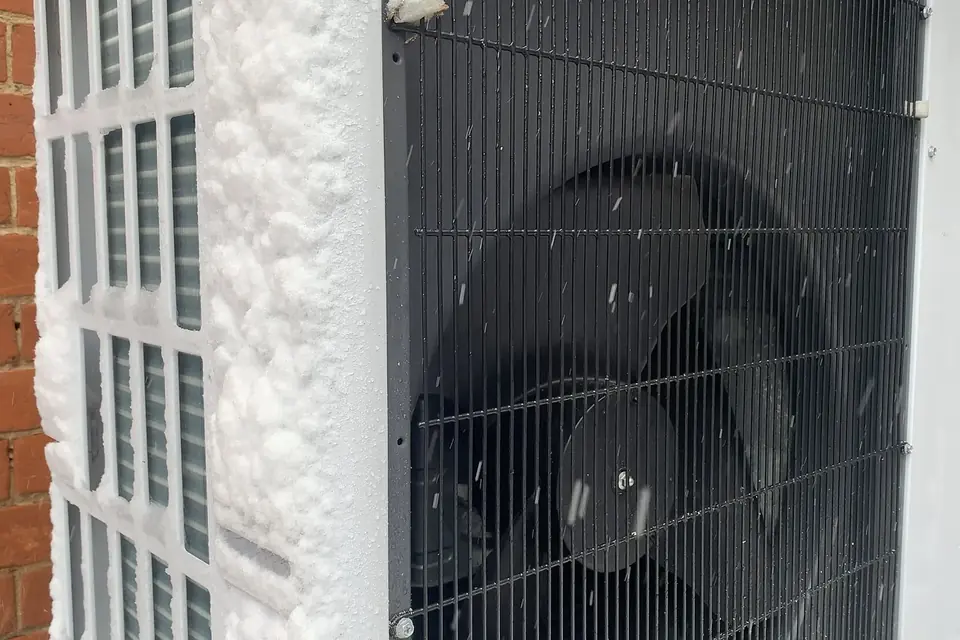 Unité extérieure de pompe à chaleur sous la neige contre un mur en brique