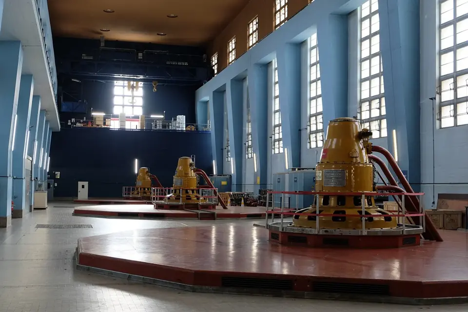 Salle des machines d'une centrale hydroélectrique avec des groupes peints en jaune sur un sol rouge et de hautes fenêtres