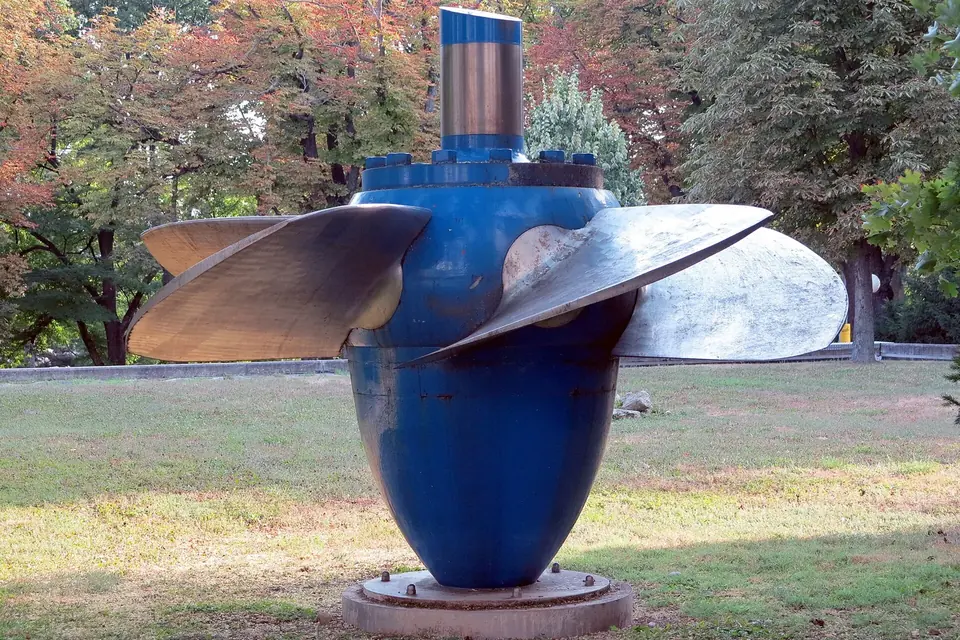 Roue de turbine Kaplan à pales orientables exposée sur un socle dans un parc